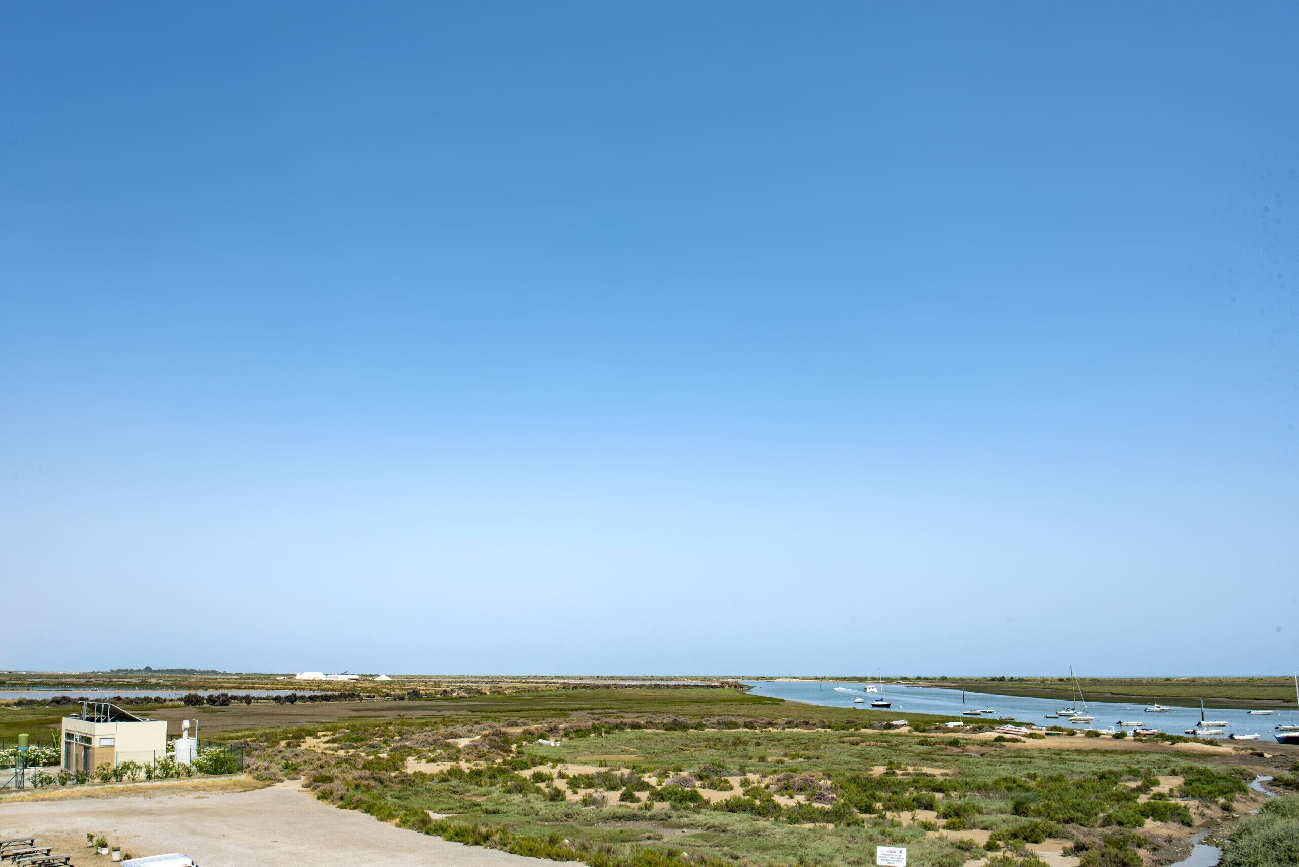 Un paisaje costero con un edificio, campos abiertos y barcos en el agua.
