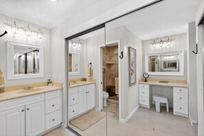A modern bathroom with a double sink vanity, a walk-in closet, and a glass shower enclosure.