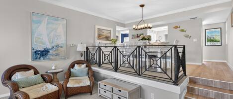 A spacious living area with a high ceiling, a staircase, and a view of the kitchen.