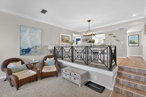 A spacious living area with a high ceiling, a staircase, and a view of the kitchen.
