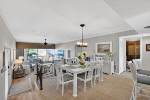 Een ruime woonkamer met een eettafel, witte stoelen, een kroonluchter en uitzicht op de omgeving.