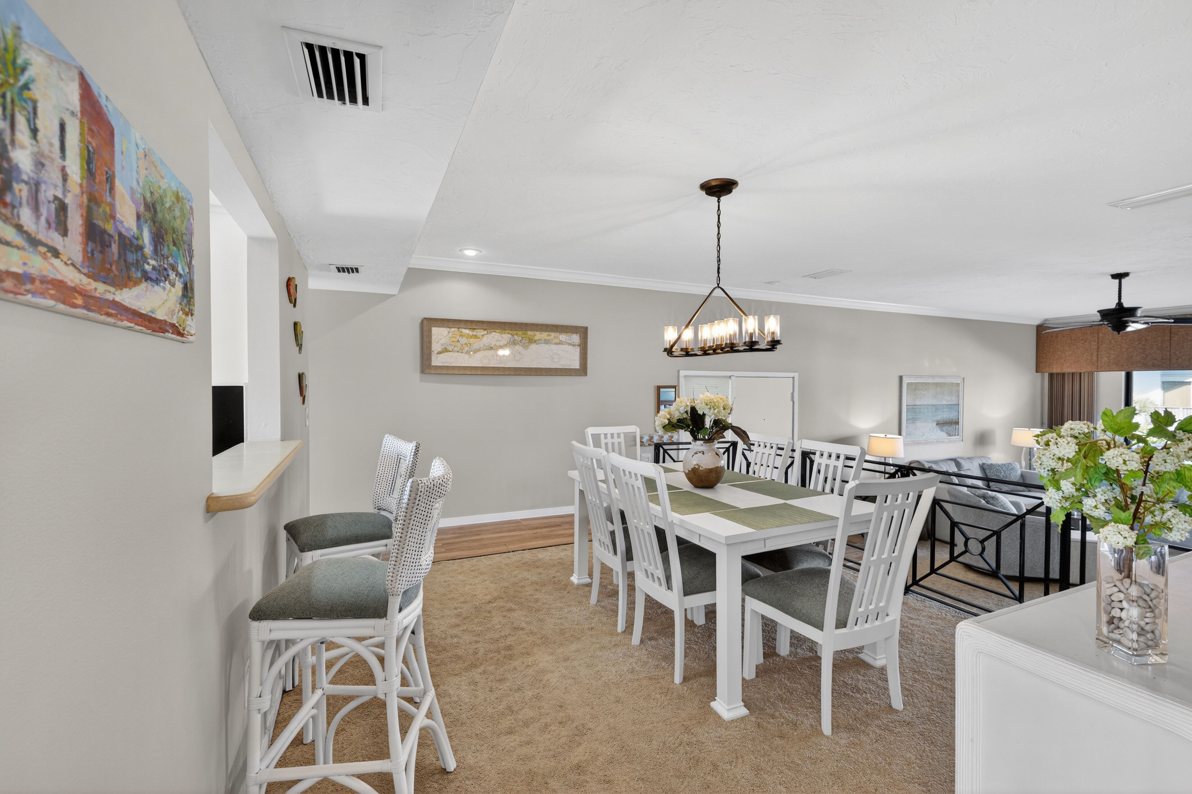 Un coin repas avec une table et des chaises blanches, un lustre et un tableau au mur.