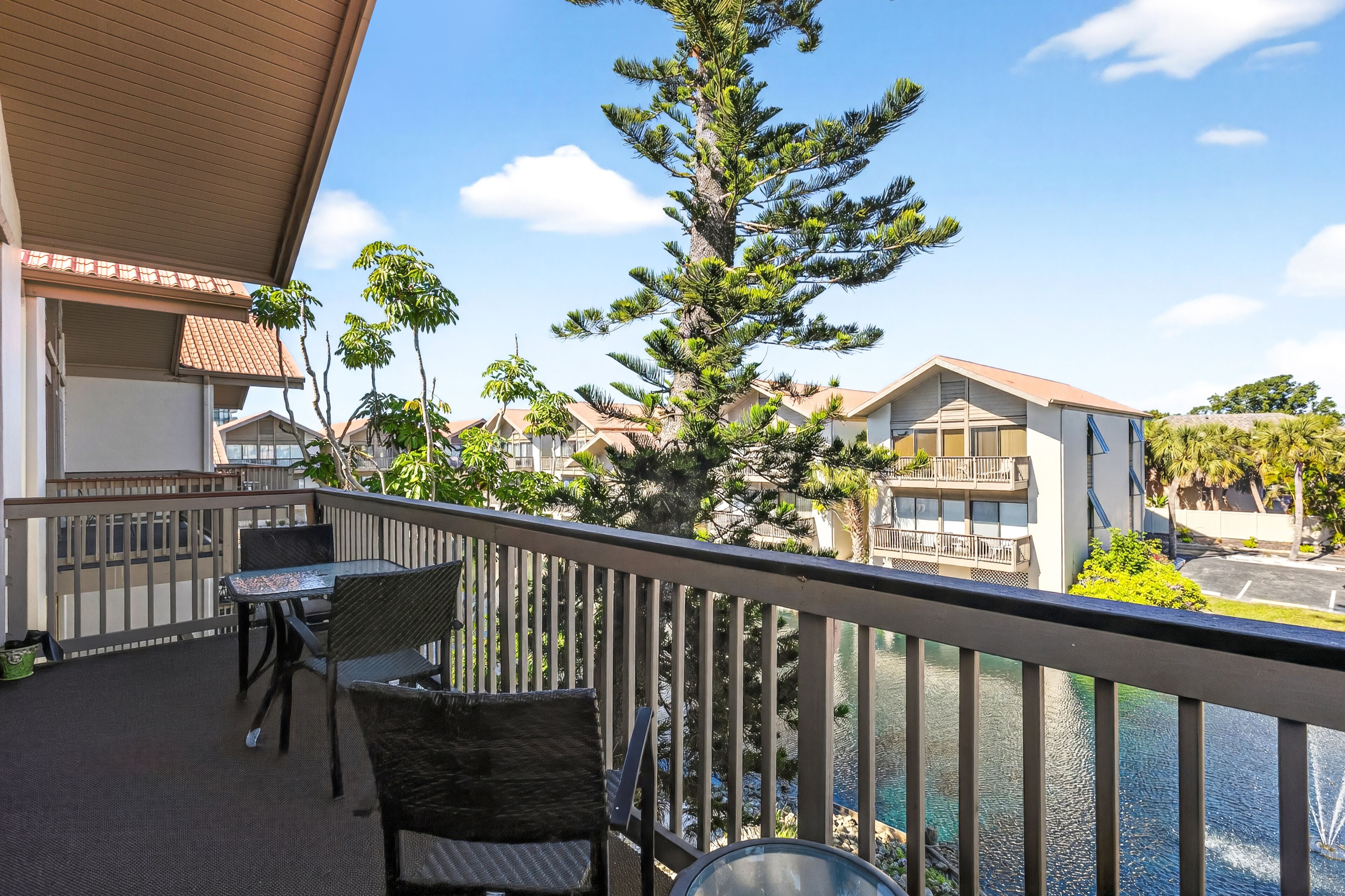 A balcony with outdoor furniture, a view of a building with a tiled roof, and a large tree.