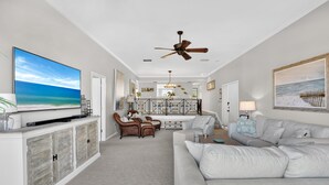 A spacious living room with a large flat-screen TV, a ceiling fan, and a dining area with a view of the ocean. - Coastal Lakehouse Condo on Siesta Key Public Beach (Siesta Key)
