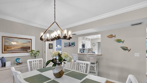 A dining area with a table set for four, white chairs, a chandelier, and wall art. - Coastal Lakehouse Condo on Siesta Key Public Beach (Siesta Key)