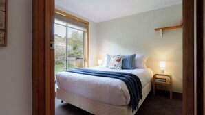 Un dormitorio con cama, mesita de noche con lámpara, ventana y puerta.