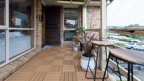 Un balcón con piso de madera, plantas en macetas y una zona de estar con mesa y sillas.