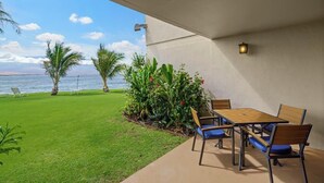 Un patio con una mesa y sillas, vista al océano y un césped bien cuidado.