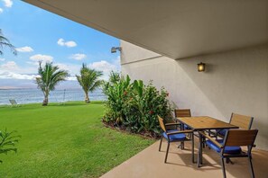 Un patio con una mesa y sillas, vista al océano y un césped bien cuidado.