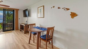 Un comedor con una mesa y sillas de madera, un televisor de pantalla plana montado en la pared y vistas al exterior a través de un ventanal corredero.