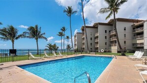 Una piscina con sillones de descanso, palmeras y un edificio con balcones.