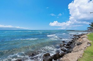 Vista costera con agua azul cristalina, costa rocosa y una cadena montañosa distante.