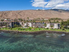 Un complejo turístico con edificios de varios pisos, un área de piscina y vistas a parques eólicos al fondo.