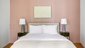 Un lit bien fait, avec du linge de lit blanc, deux tables de chevet avec des lampes, et un mur sobre orné d’une seule œuvre d’art au-dessus du lit.