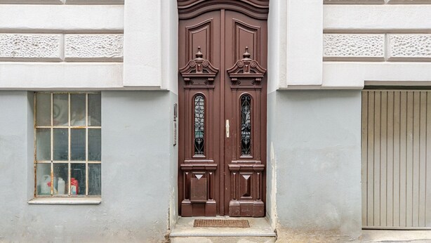 Une porte à deux battants de couleur marron, ornée d’éléments décoratifs et dotée d’une petite fenêtre sur le côté gauche.