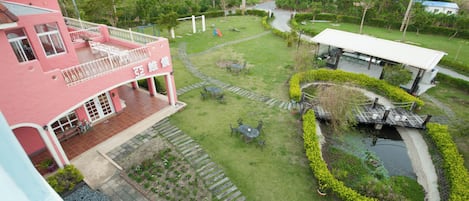 Un edificio rosa con un balcón, un pequeño jardín con un estanque y una estructura blanca al fondo.
