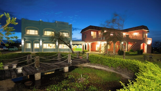 A two-story building with a bridge over a water feature, surrounded by greenery.
