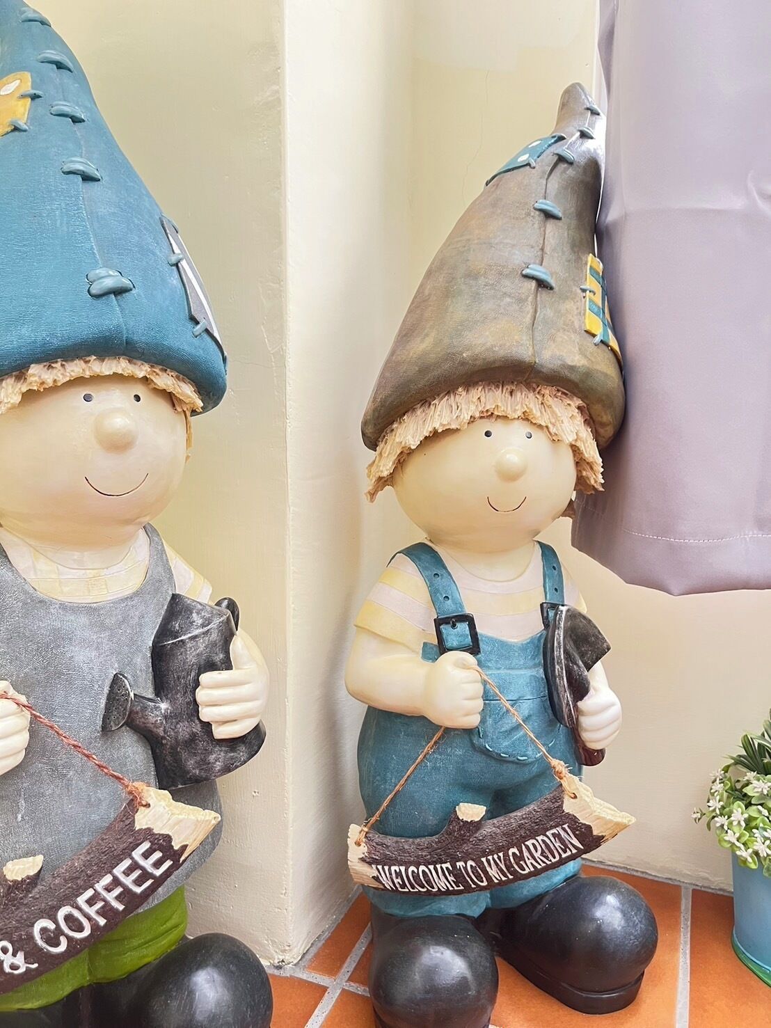 Dos estatuillas de gnomos de jardín, uno sosteniendo un martillo y el otro un letrero que dice 'Bienvenido a mi jardín'.
