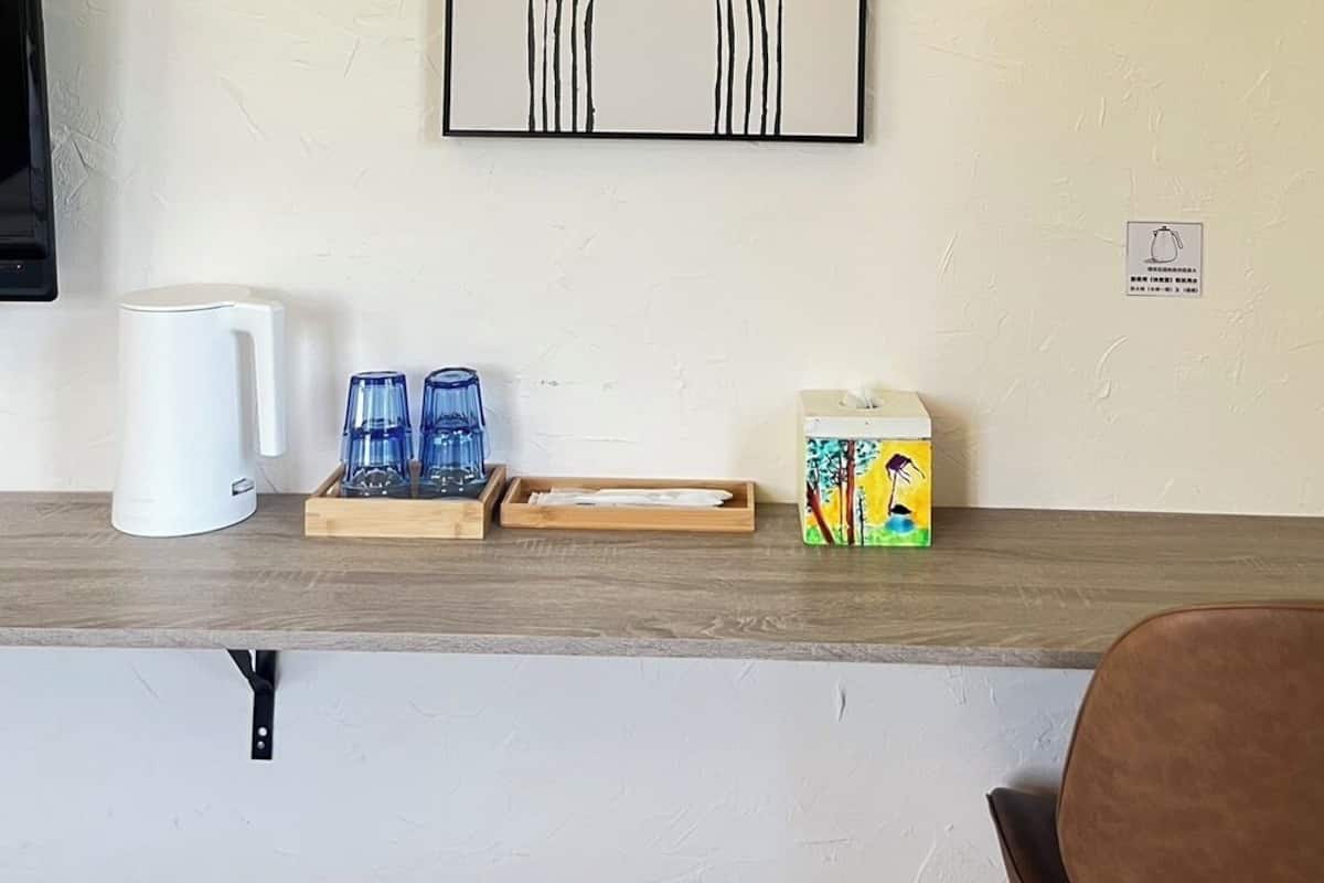 A wall-mounted abstract art piece, a white coffee maker, and a tray with blue glasses and a carton of milk on a wooden counter.