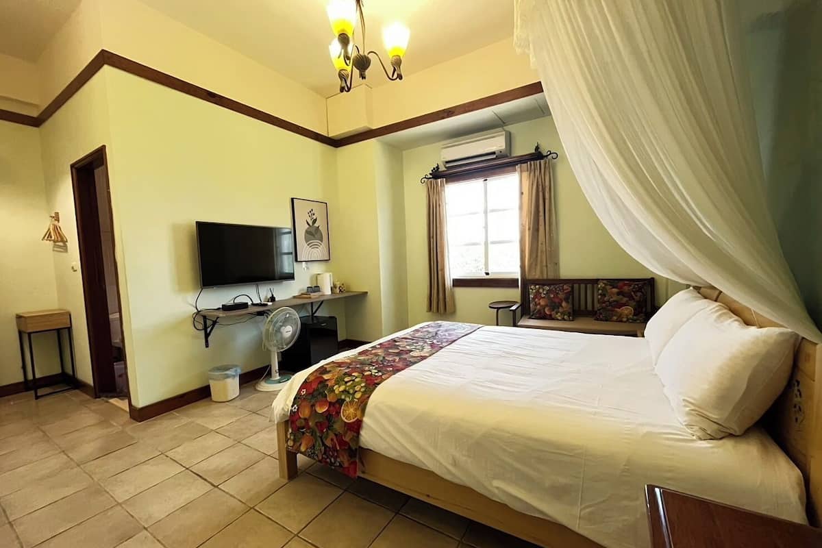 A bedroom with a bed, a television, a desk, and a window with curtains.