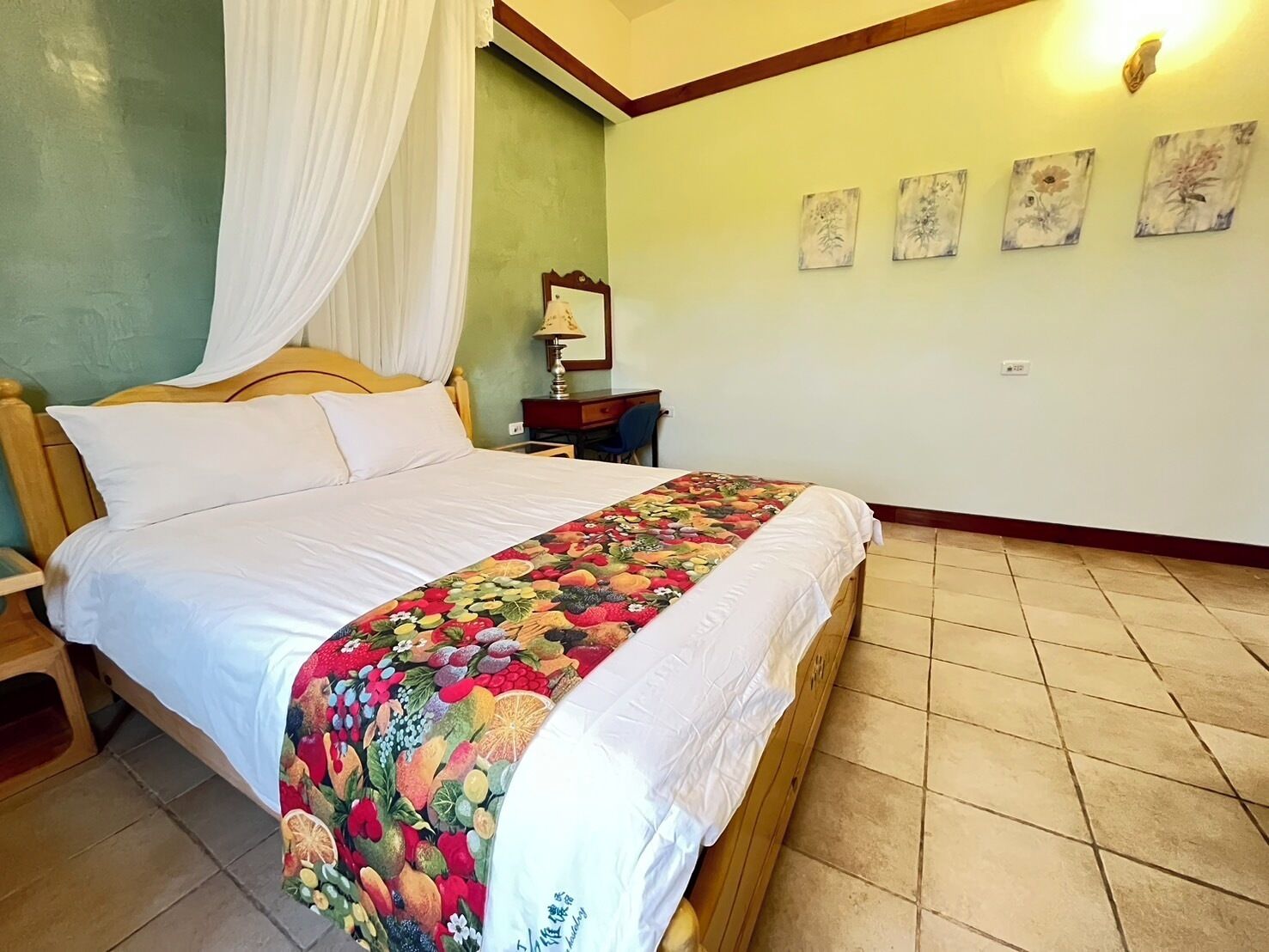 A bedroom with a bed, a nightstand, a lamp, and a wall with four framed pictures.
