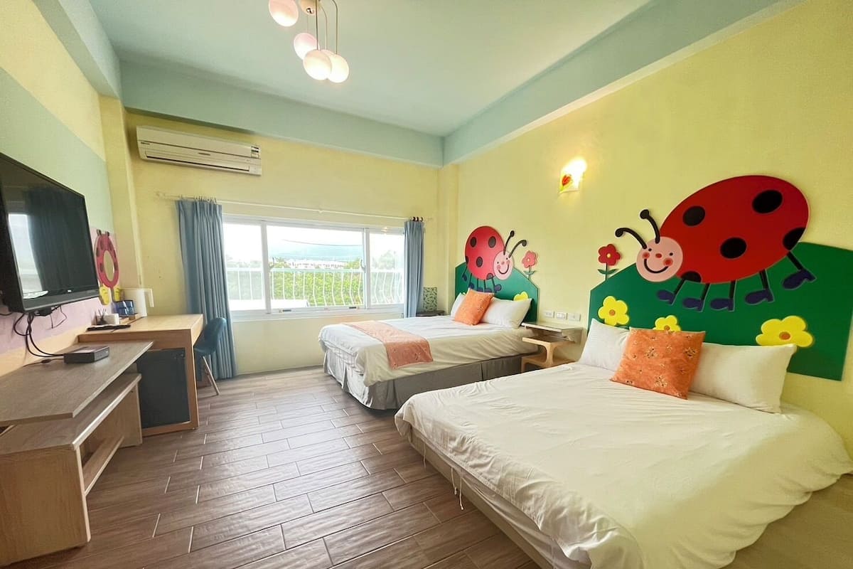 A hotel room with two beds, a TV, a desk, and a window with a view.