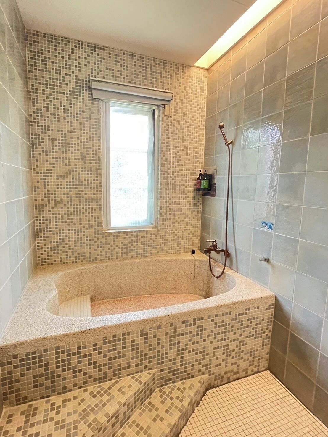 Un baño con pared de mosaicos, una ventana, una bañera y una zona de ducha.