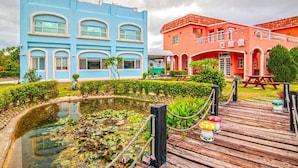 A hotel with a blue building and a red building, both with multiple windows and a garden area with a pond and wooden deck.