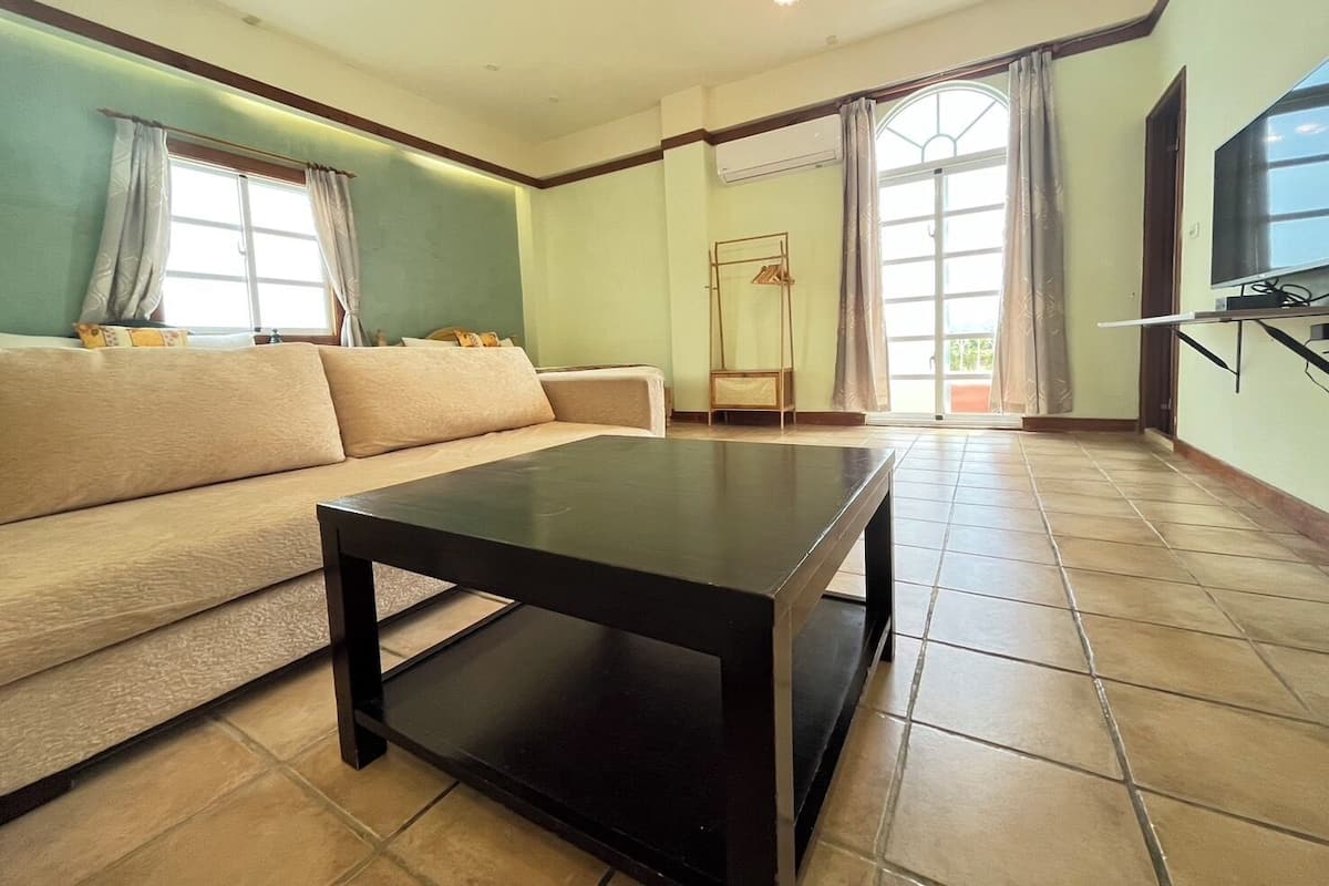 A living room with a sofa, a coffee table, a TV, and a window with curtains.
