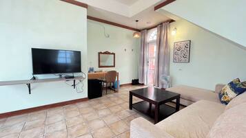 A living room with a TV, a desk, a chair, a sofa, and a small table.