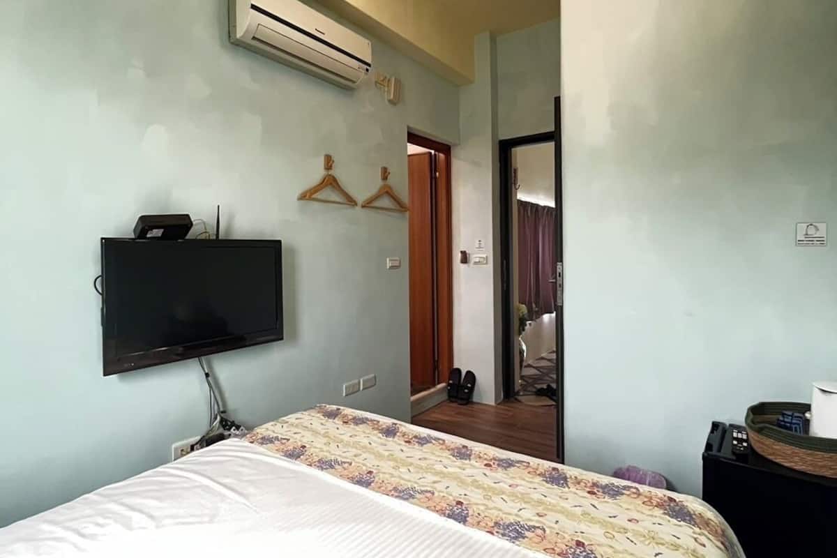 A bedroom with a bed, a TV, an air conditioner, and a door leading to another room.
