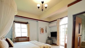 A bedroom with a bed, a desk, a chair, a TV, and a window.
