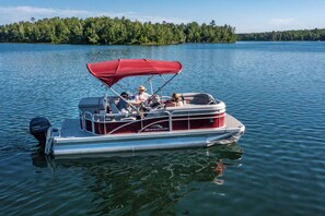 A motorboat with a red canopy, passengers, and a forested shoreline in the background. - Tiny RV with amazing lake view! (Nevis)