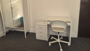 Et lille, hvidt kontor med et skrivebord og stol, et skab med skuffer og et tæppe på gulvet.
