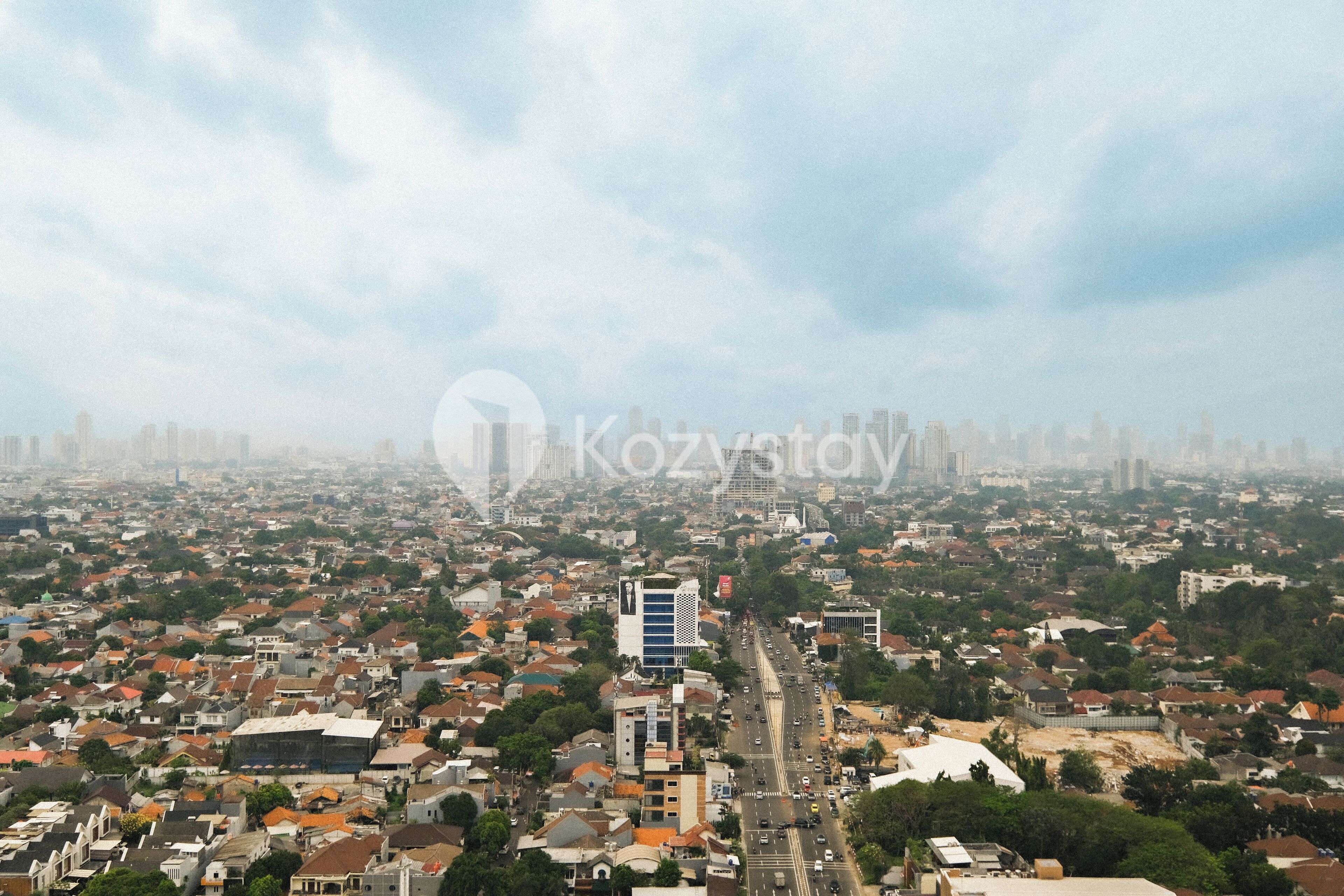 Un paisaje urbano con una mezcla de edificios residenciales y comerciales, un edificio moderno destacado en el centro, y una amplia avenida que lo atraviesa.