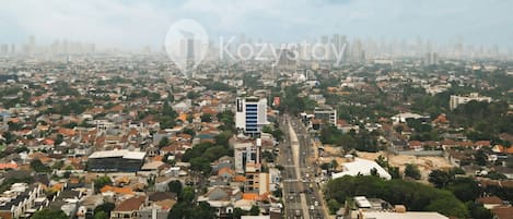 Un paisaje urbano con una mezcla de edificios residenciales y comerciales, un edificio moderno destacado en el centro, y una amplia avenida que lo atraviesa.