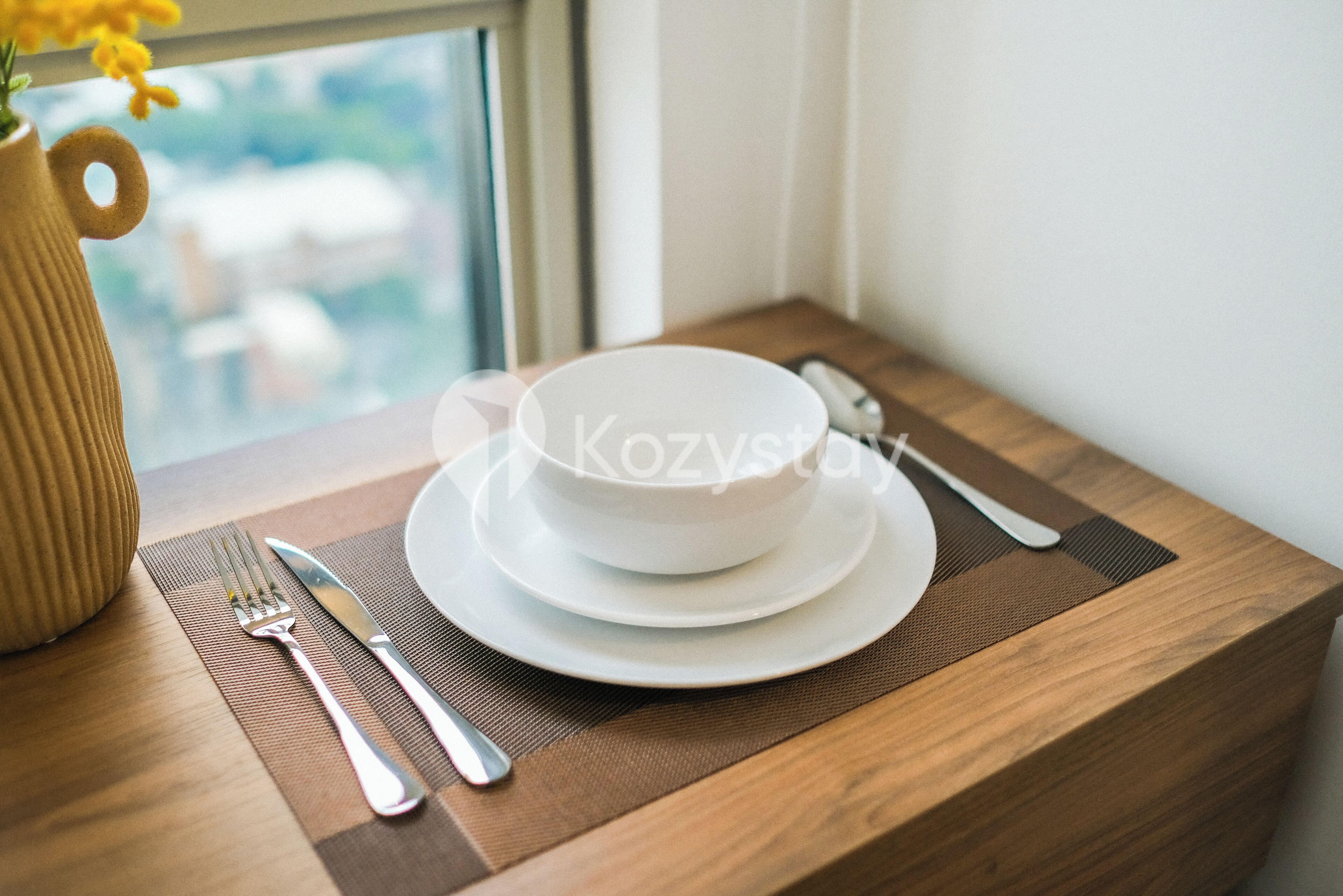 Een eettafel met een wit bord, kom en bestek, in de buurt van een raam.