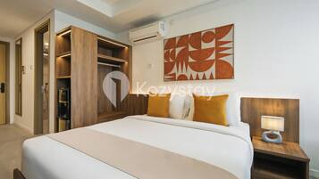 A hotel room with a large bed, a wooden wardrobe, a wall-mounted air conditioner, and a modern abstract painting.