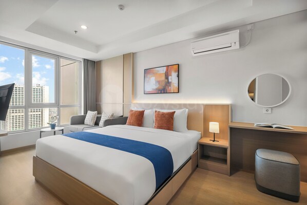 A modern hotel room with a large bed, a desk, a chair, a TV, and a window with a city view. - Staya Antasari by Kozystay - Cilandak (Jakarta)