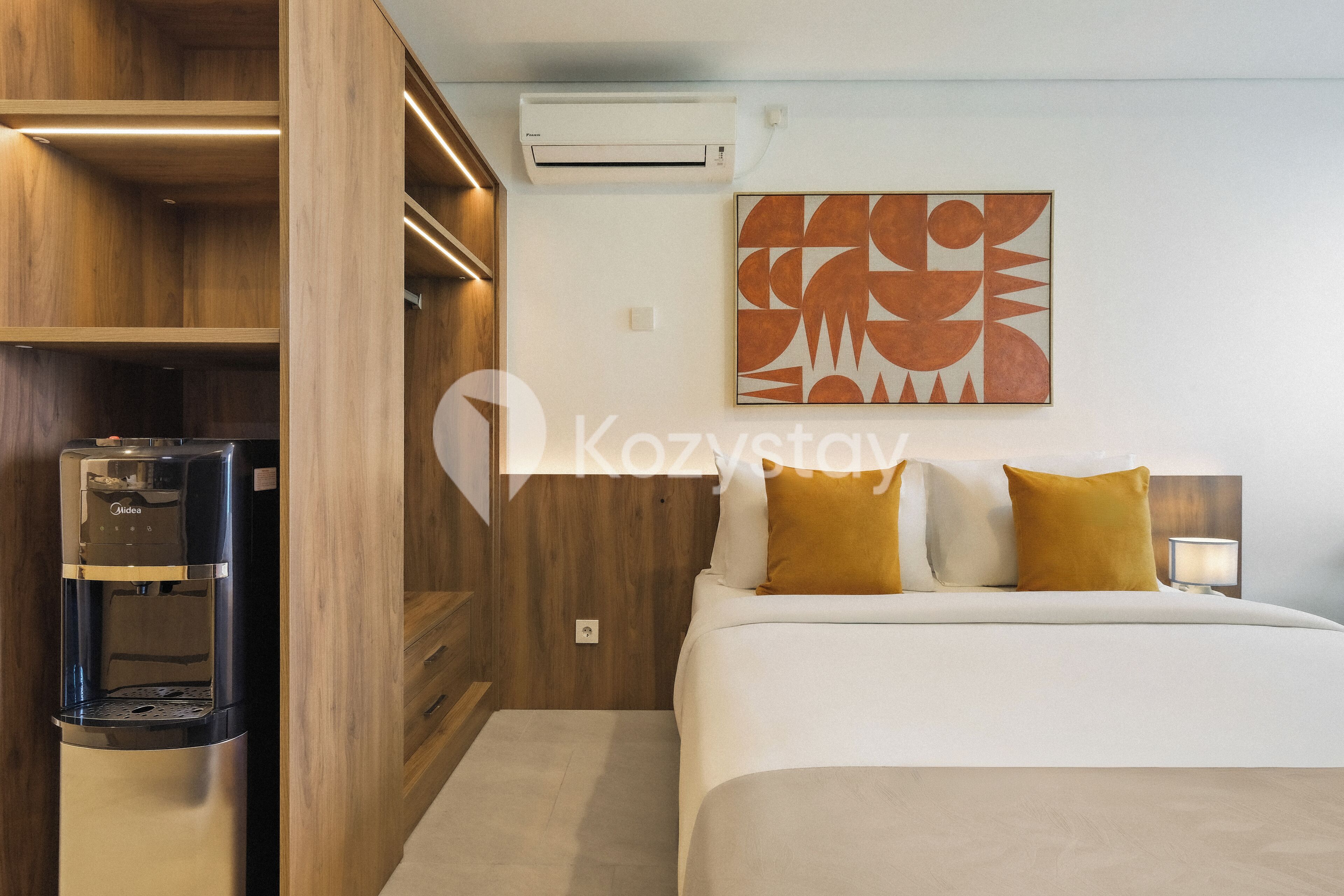 A hotel room with a bed, a water dispenser, a wall-mounted air conditioner, and a geometric artwork.