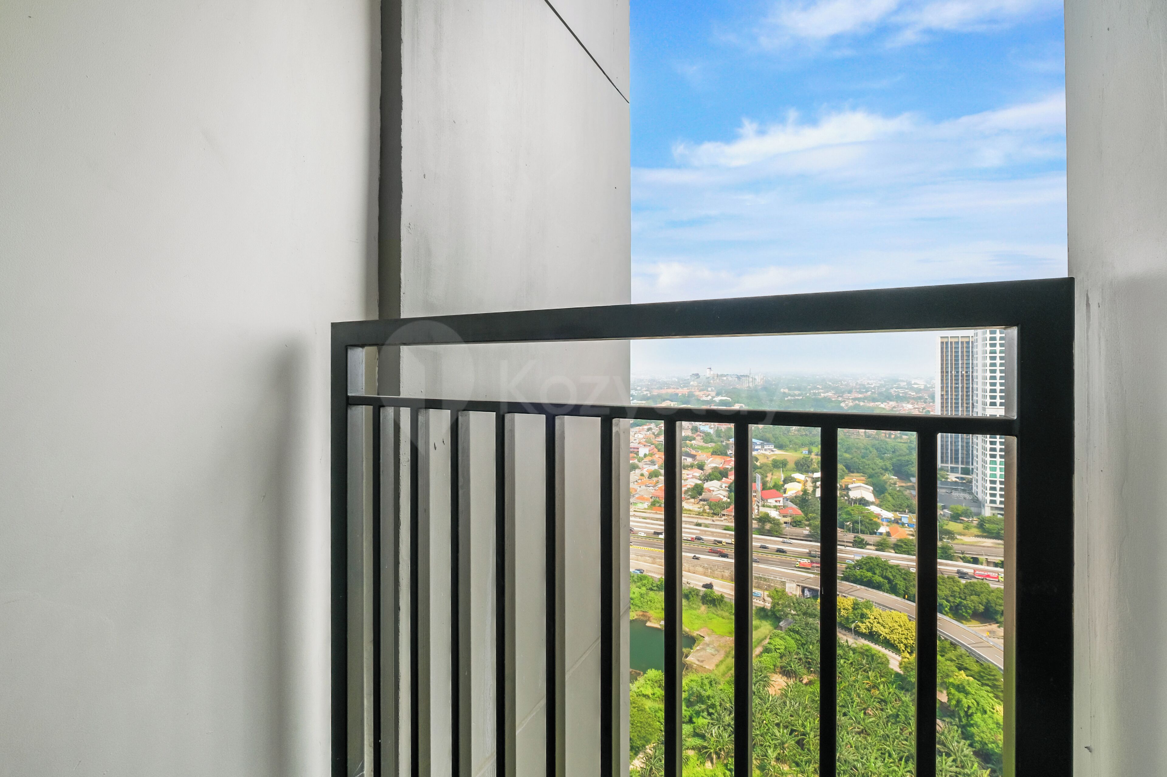 Een balkon met een metalen hekwerk met uitzicht op een stadsbeeld met gebouwen en groen.