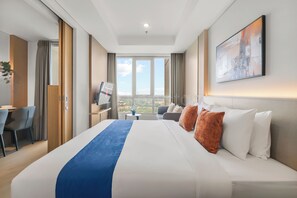 A hotel room with a large bed, a desk, a chair, a TV, and a window with a city view.