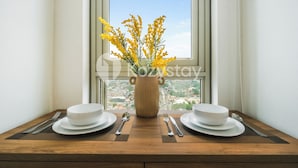 A dining table with white plates, silverware, and a vase with yellow flowers by a window. - Staya Antasari by Kozystay - Cilandak (Jakarta)