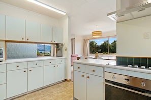 A modern kitchen with light-colored cabinets, a built-in oven, and a view of the outdoors.