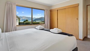A hotel room with a large bed, a view of mountains and a lake, and a wooden wardrobe.