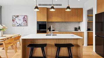 A modern kitchen with wooden cabinets, a white countertop, and two black barstools.