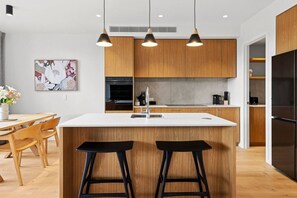A modern kitchen with wooden cabinets, a white countertop, and two black barstools.