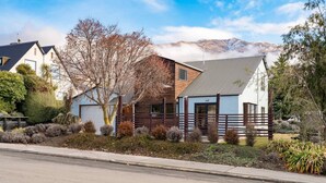 A modern house with a sloped roof, a wooden deck, and a well-maintained garden. - Wanaka close to town | Modern | Fireplace & Heatpumps | Sleeps 6 (Wānaka)