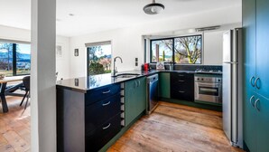A modern kitchen with a large island, built-in appliances, and a view through the window. - Wanaka close to town | Modern | Fireplace & Heatpumps | Sleeps 6 (Wānaka)
