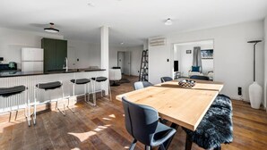 A modern kitchen with a central island, bar stools, and a dining table with chairs. - Wanaka close to town | Modern | Fireplace & Heatpumps | Sleeps 6 (Wānaka)